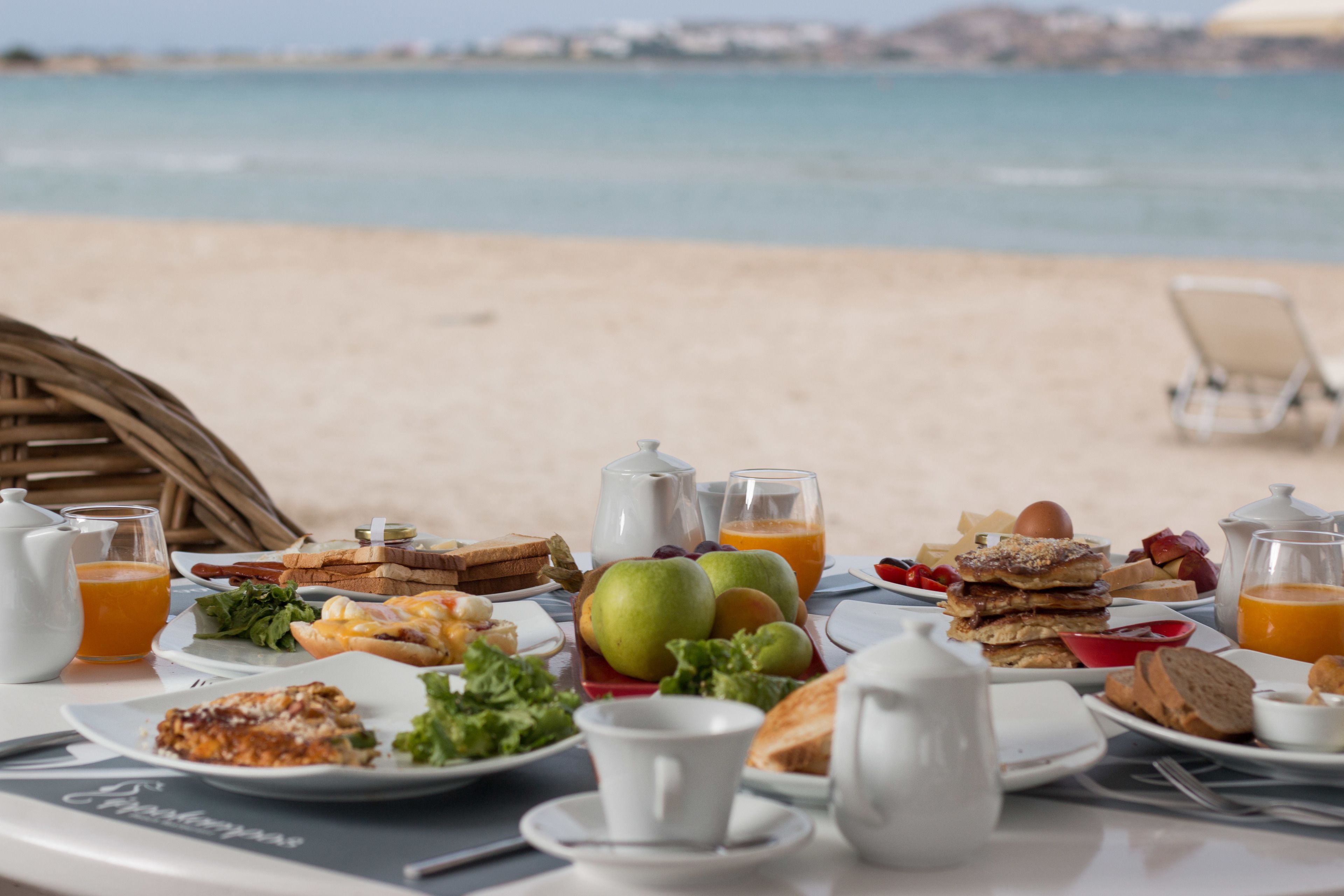 A breakfast table with various food items and a view of the beach.