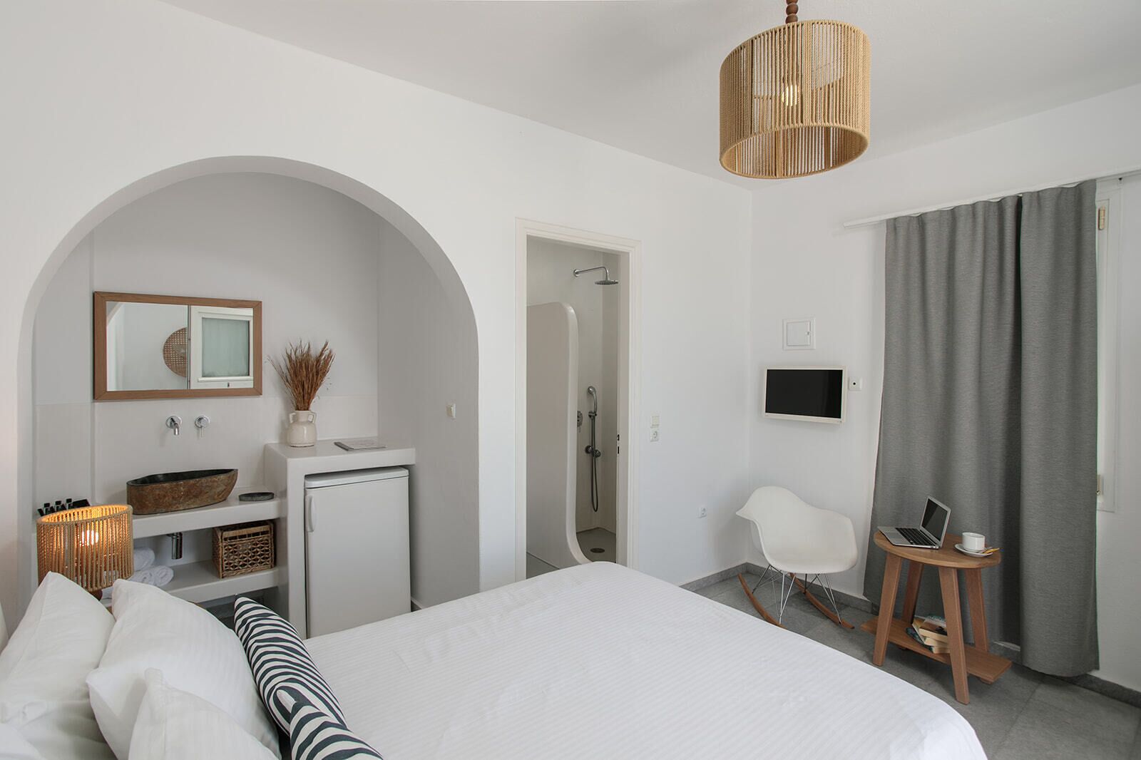 Una habitación de hotel moderna con una cama grande, un escritorio pequeño con una computadora portátil, un televisor y una zona de ducha.