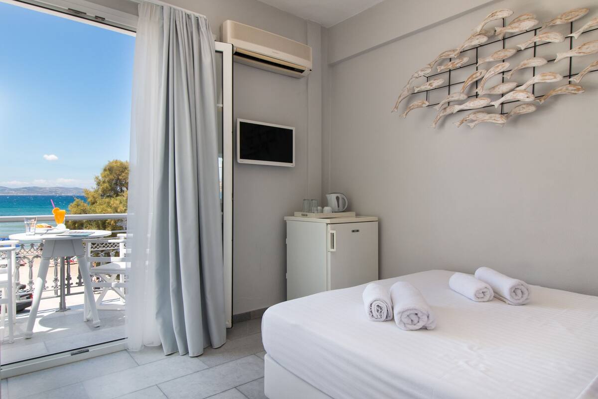 A hotel room with a bed, a small refrigerator, a flat-screen TV, and a balcony with a table and chairs.