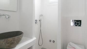 Ein modernes Badezimmer mit einem weißen Waschbecken, einem großen Spiegel, einer Dusche inklusive Handbrause und einer Toilette.