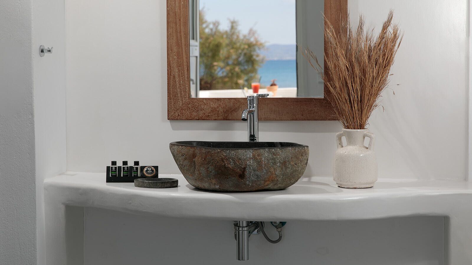Un baño con un lavamanos de piedra, un espejo y un florero con plantas secas.