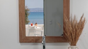 A bathroom with a stone sink, a mirror reflecting a view of the sea, and a vase with dried plants. - Ippokampos Beachfront (Naxos)
