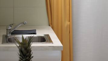 A kitchen with a sink, a window with yellow curtains, and a table with fruits.