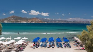 A beach with rows of blue umbrellas and sun loungers, a clear blue sea, and distant mountains. - Ippokampos Beachfront (Naxos)