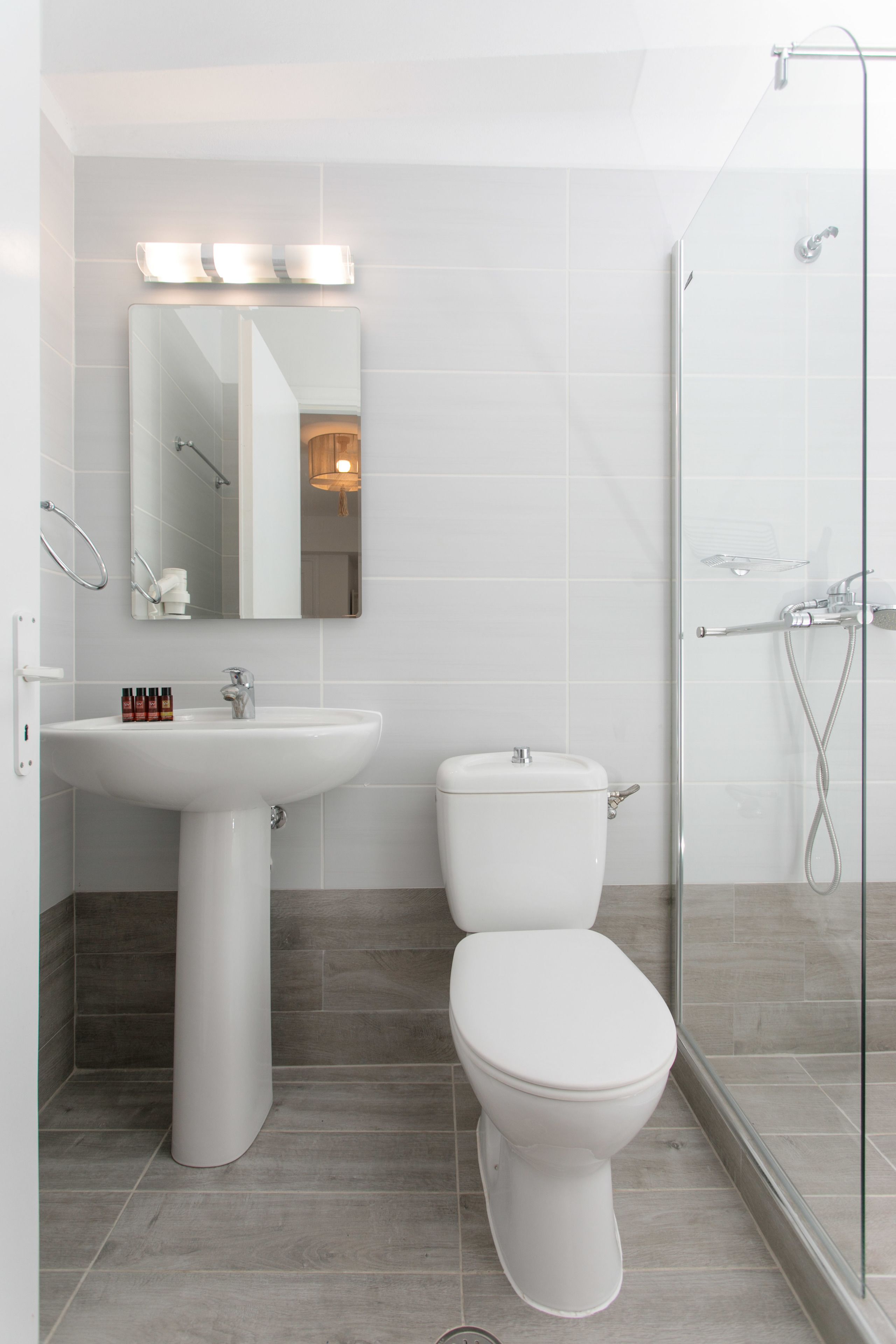 Un bany modern amb un lavabo blanc, un vàter i una dutxa amb envàs de vidre.