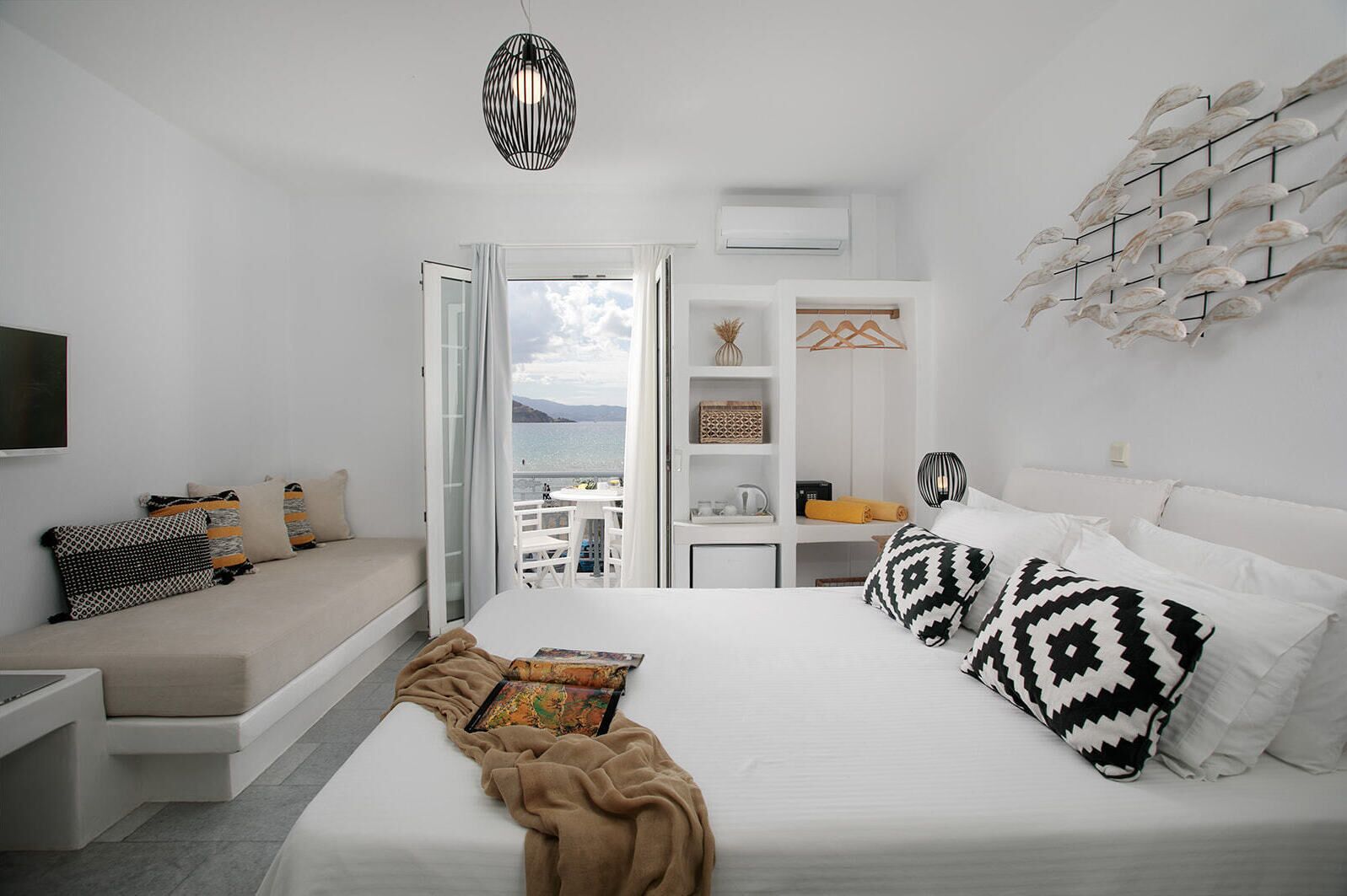 A modern bedroom with a large bed, a sofa, and a balcony with a view.
