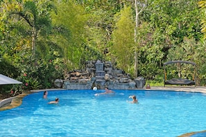 Ein Schwimmbecken, umgeben von üppiger Vegetation und einem Wasserfall.
