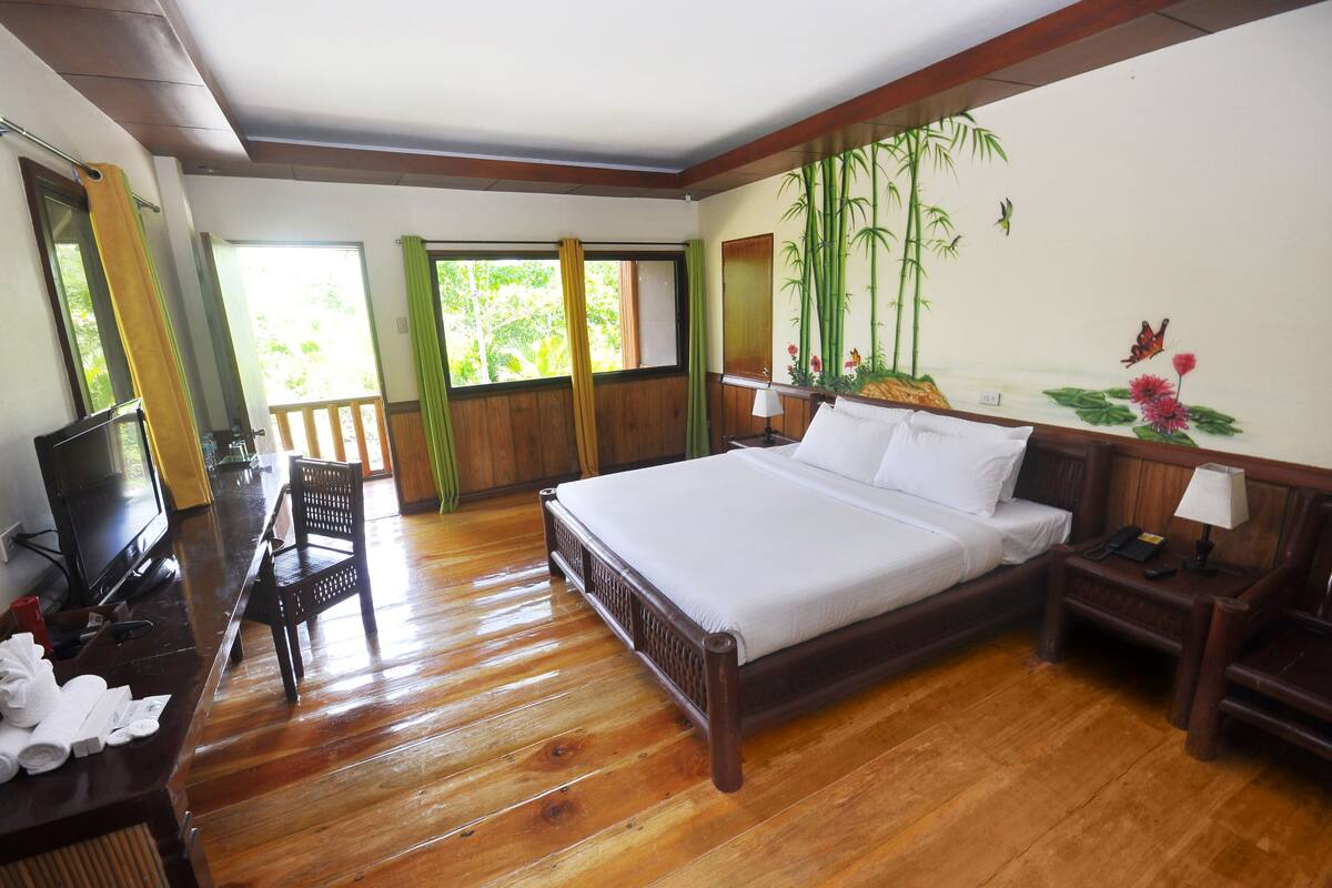 A hotel room with a wooden bed, a desk with a TV, a chair, and a window with curtains.
