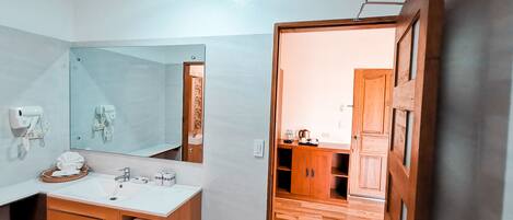 Une salle de bain moderne avec un grand miroir, un meuble-lavabo en bois et une porte en bois donnant sur un coin cuisine.
