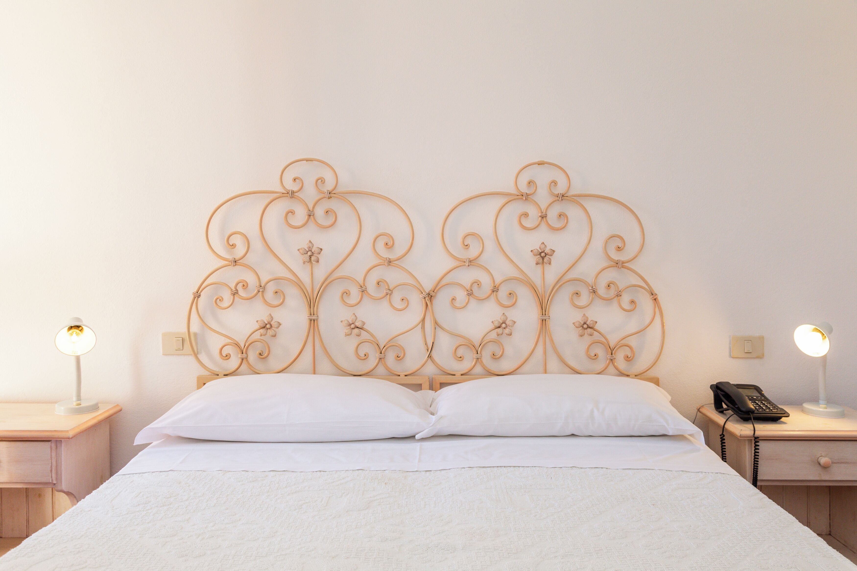 A neatly made bed with a decorative metal headboard, two bedside lamps, and a bedside telephone on a wooden nightstand.