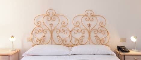 A neatly made bed with a decorative metal headboard, two bedside lamps, and a bedside telephone on a wooden nightstand.