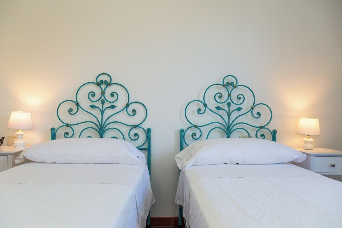 Two twin beds with teal metal headboards, white bedding, and bedside lamps.