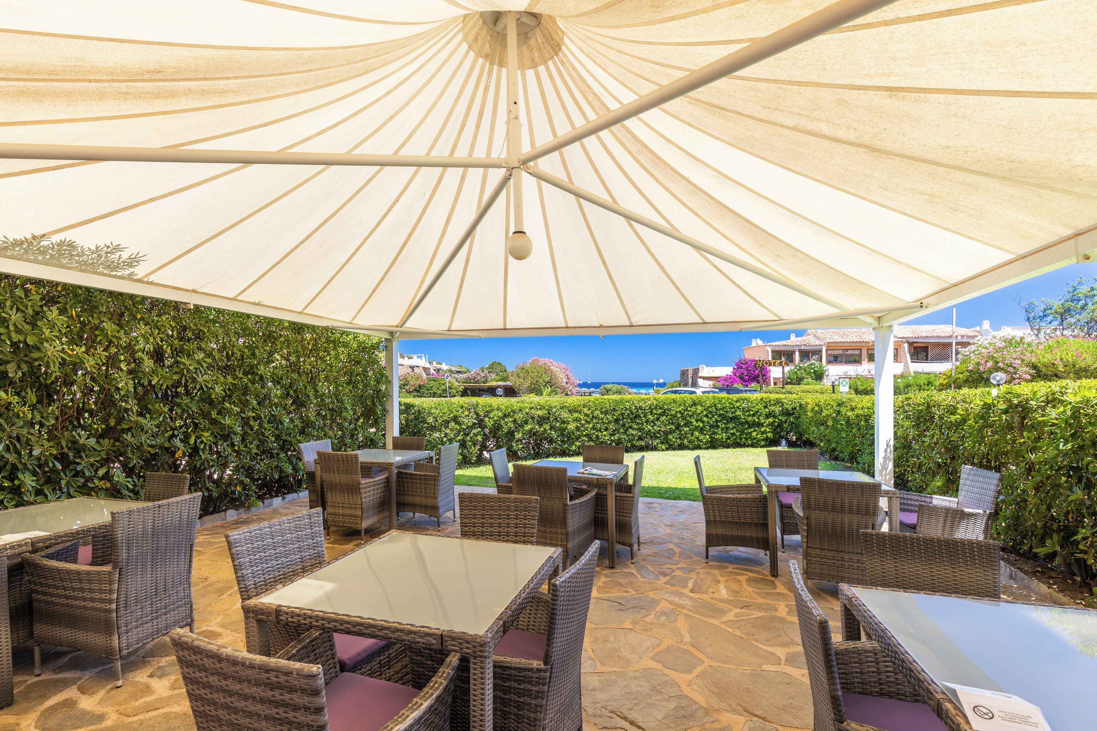 Een terras buiten met rieten meubilair en een grote parasol voor schaduw.