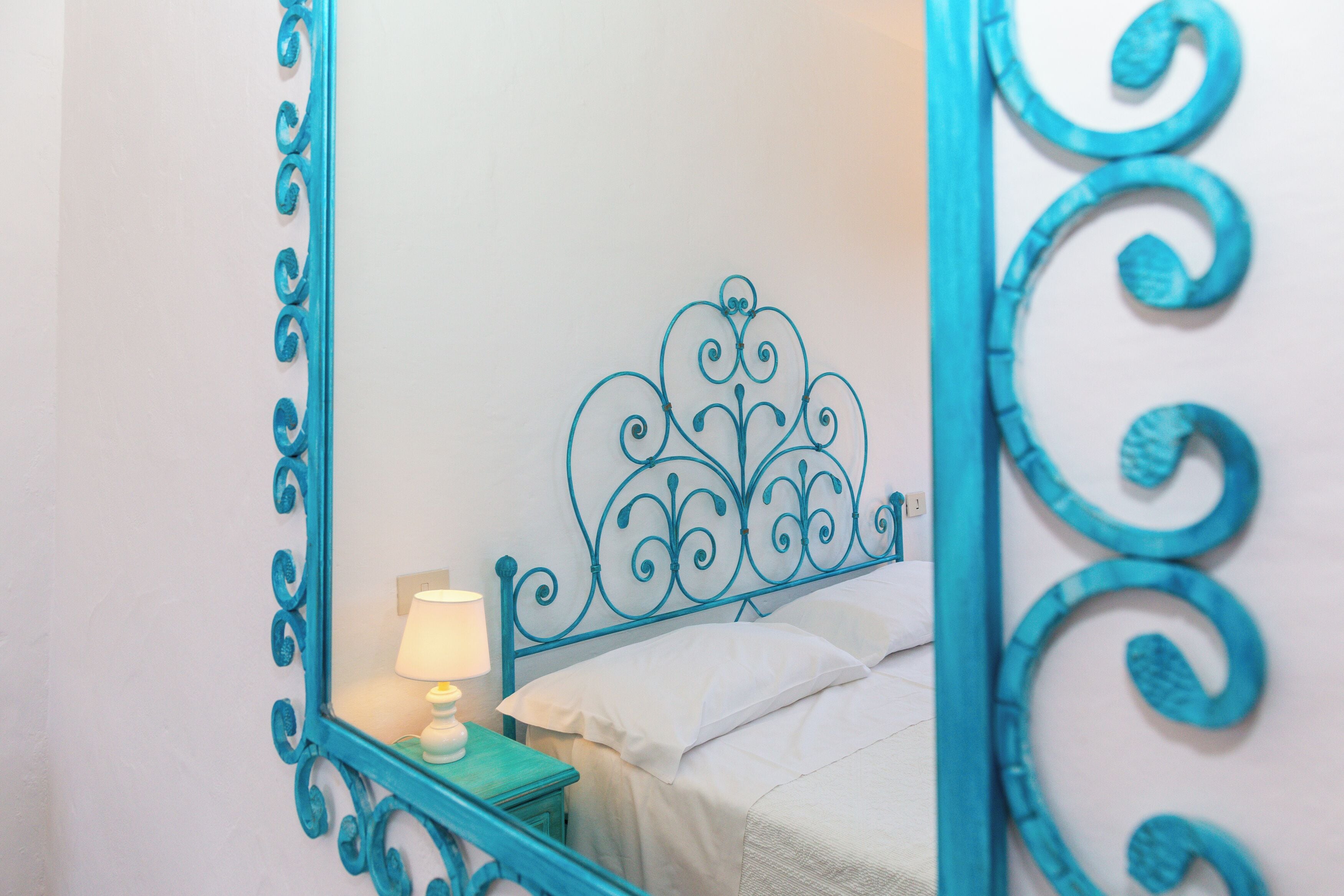A bed with a decorative headboard, a bedside table with a lamp, and a mirror with a blue frame.
