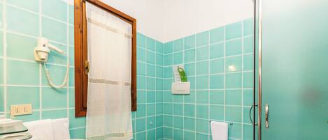 A bathroom with turquoise tiles, a white sink, a toilet, a bidet, a shower with a glass door, and a hairdryer on the wall.