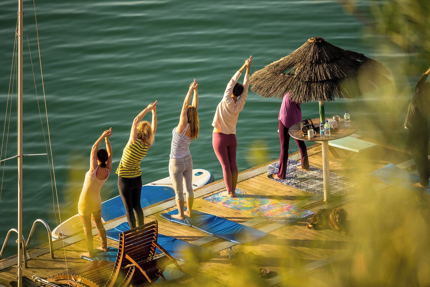 Een groep mensen doet yoga op een houten terras aan het water.