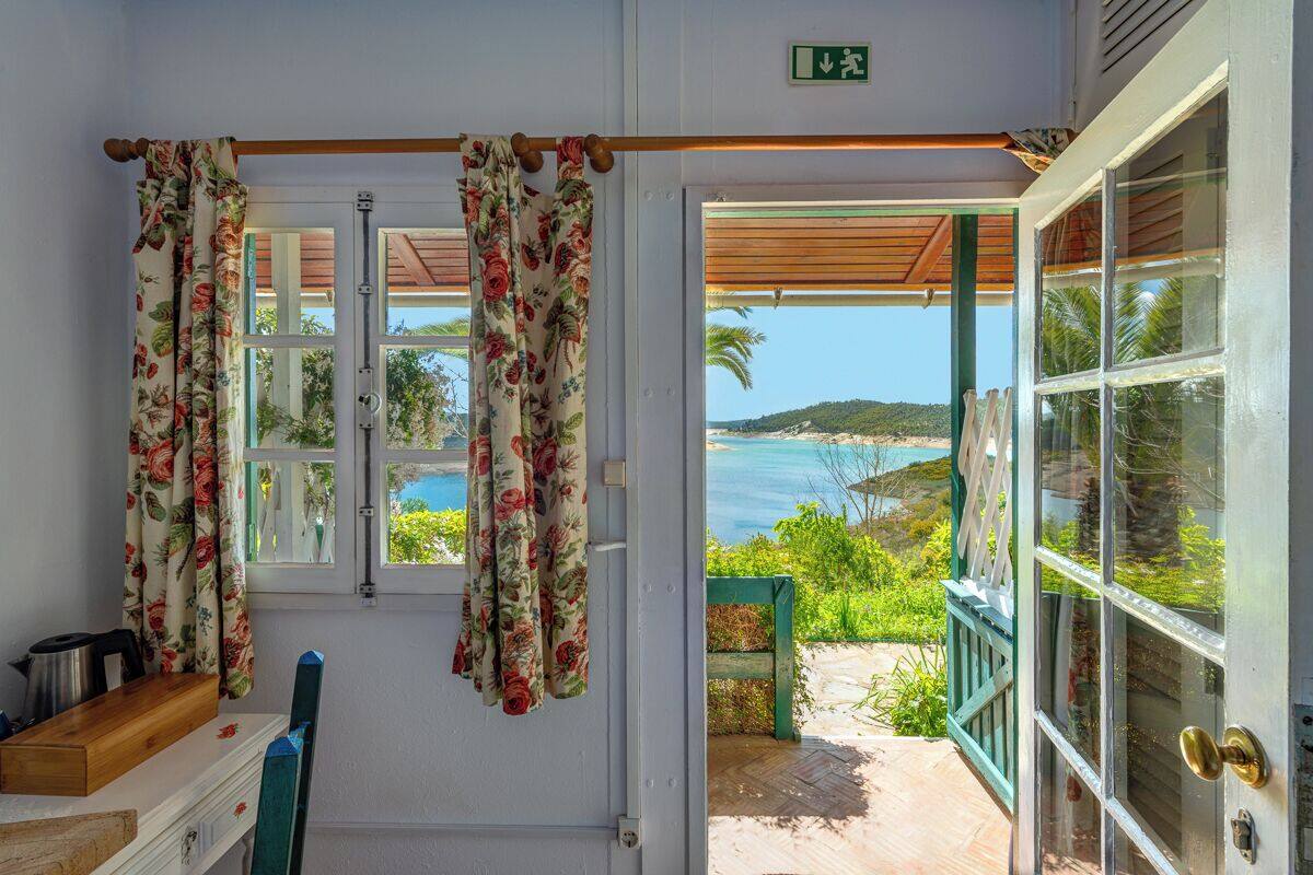 A room with a wooden table, a chair, and a view of the sea through a door.