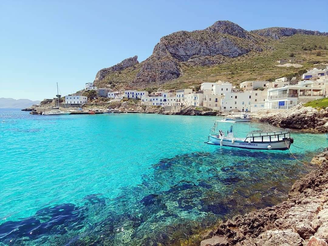 Een kustdorp met helder turquoise water, boten en witte gebouwen.