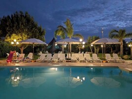 Una piscina con lettini e ombrelloni, circondata da palme e un cielo notturno.