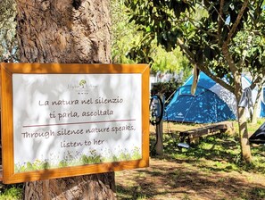 A sign with a message about nature's voice in silence, placed on a tree stump in a campsite with tents in the background. - Lilybeo Village - Camping & Residence (Marsala)