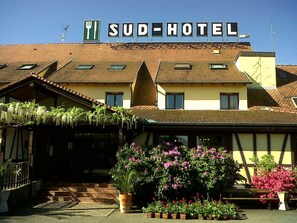 A Sud- Hotel with a traditional European architectural style, featuring a tiled roof and a welcoming entrance with potted plants and flowers. - Sud Hôtel (Huttenheim)