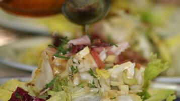 A hand pouring dressing onto a salad.