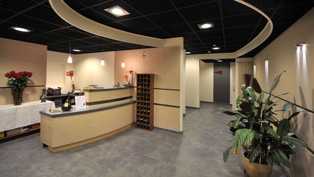 A reception area with a curved reception desk, a wine rack, and potted plants. - Sud Hôtel (Huttenheim)