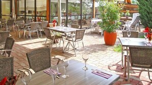 An outdoor café with wicker furniture, potted plants, and a brick floor. - Sud Hôtel (Huttenheim)