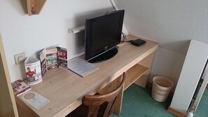 A wooden desk with a Samsung monitor, a smartphone, brochures, and a chair. - Sud Hôtel (Huttenheim)