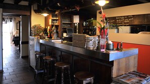 A bar area with stools, a counter, and various bottles and glasses. - Sud Hôtel (Huttenheim)