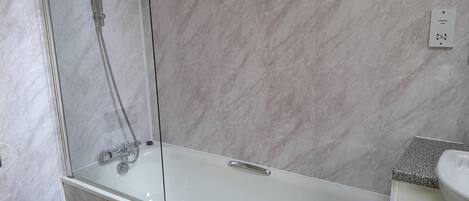 Een moderne badkamer met een douchecabine van glas, een witte badkuip en een wastafel met een granieten blad.