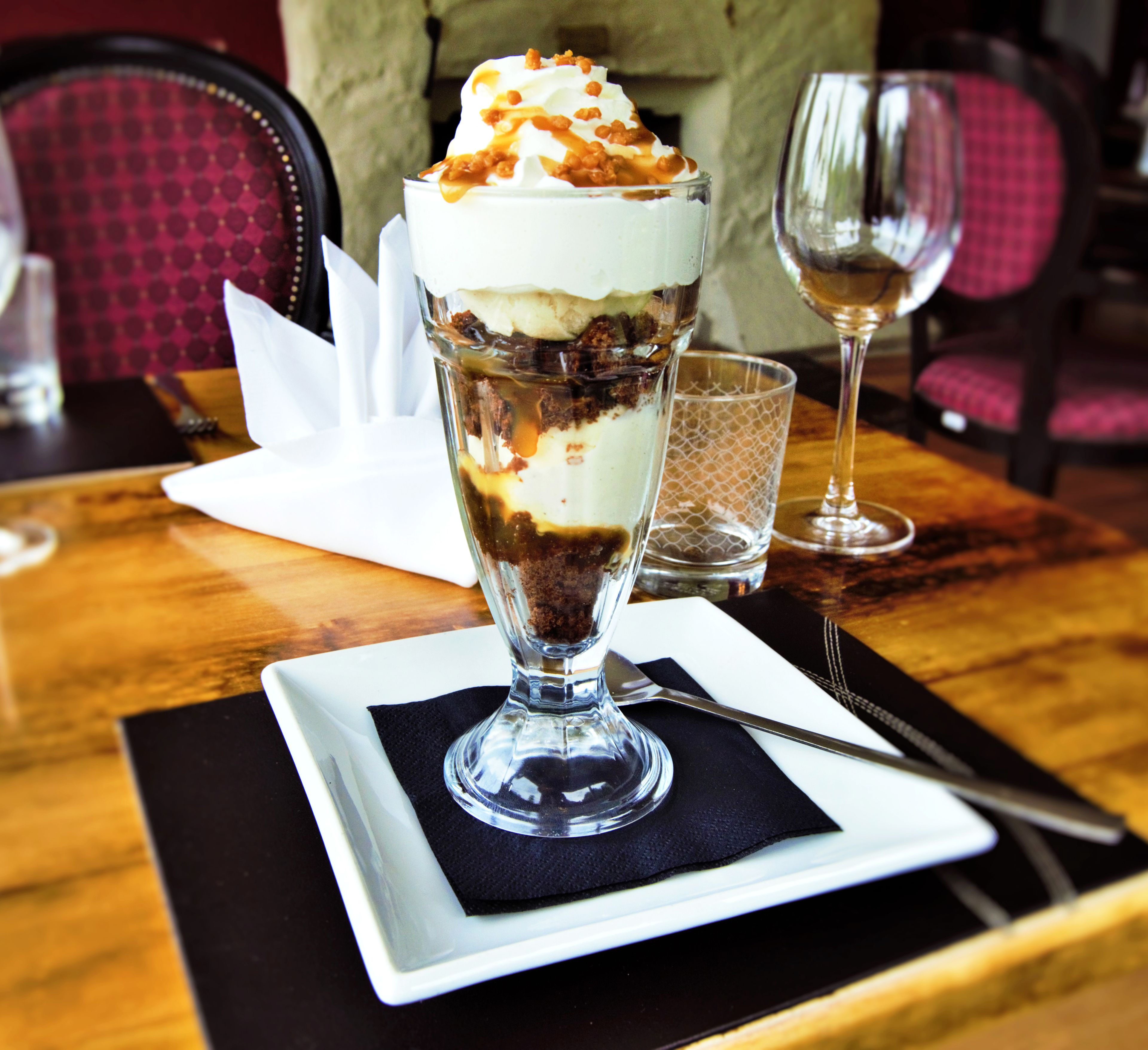 Un postre en un vaso transparente sobre un plato blanco con una servilleta negra debajo.