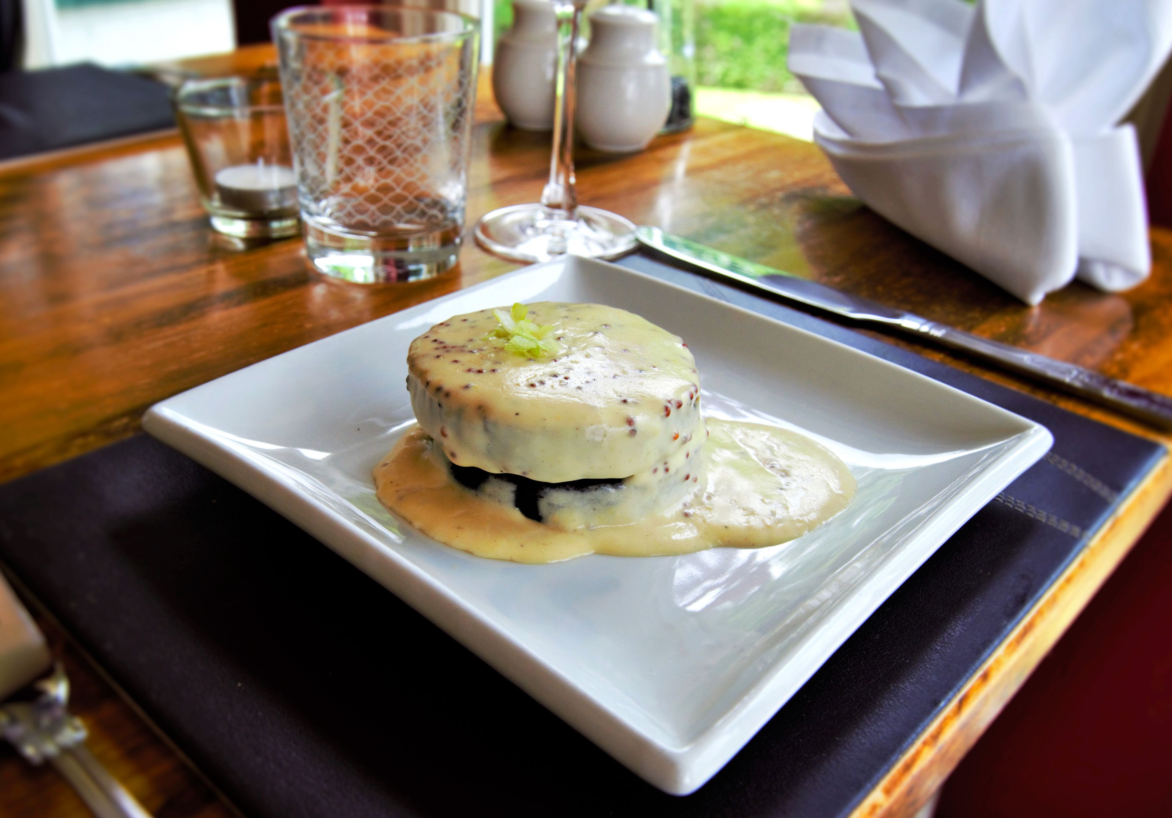A dessert on a white plate with a square base, accompanied by a glass of water and a salt shaker on a wooden table.