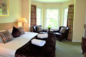 Habitación de hotel con una cama grande, dos sillones, una mesita y una ventana con cortinas.