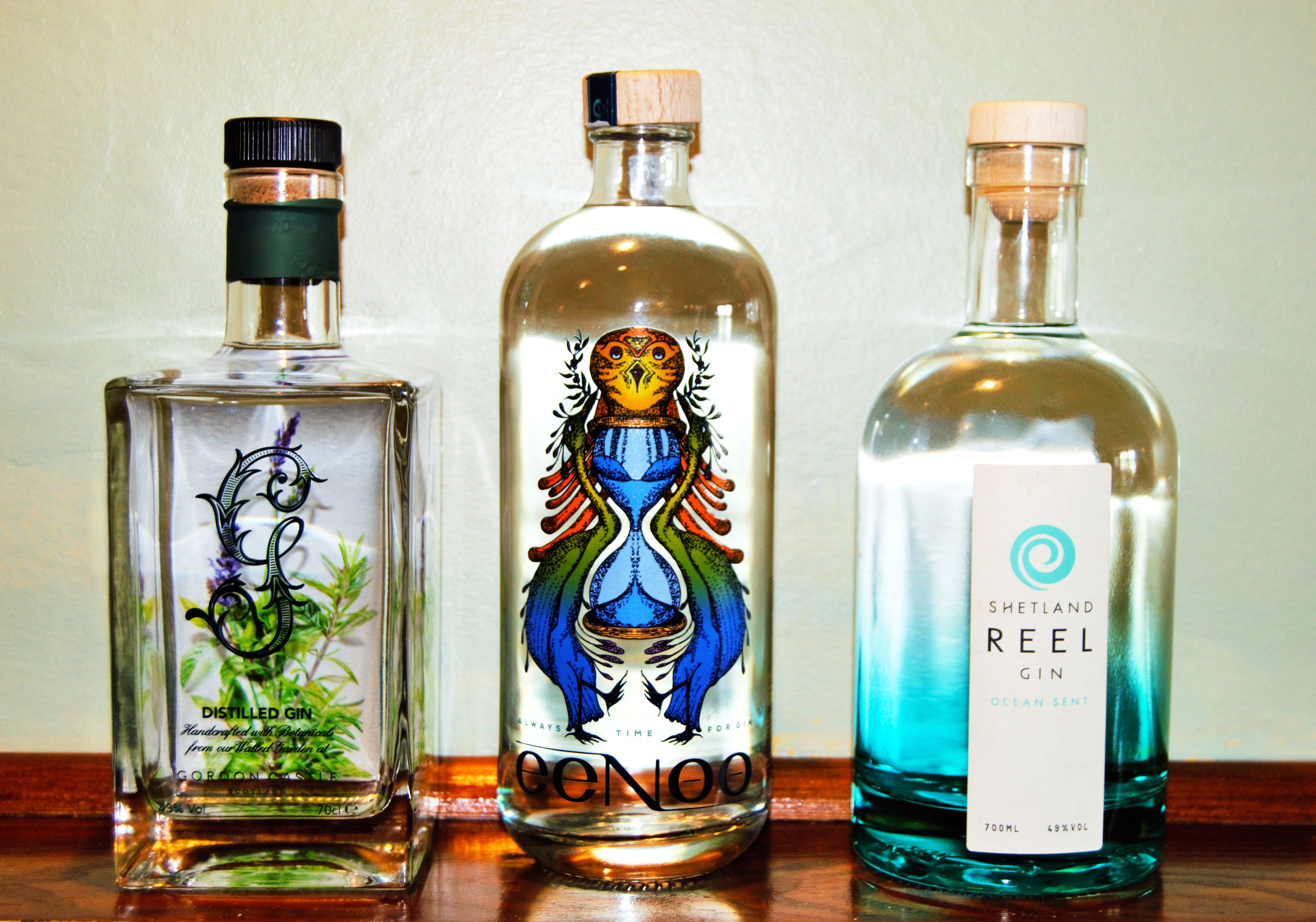 Three bottles of gin on a wooden surface.
