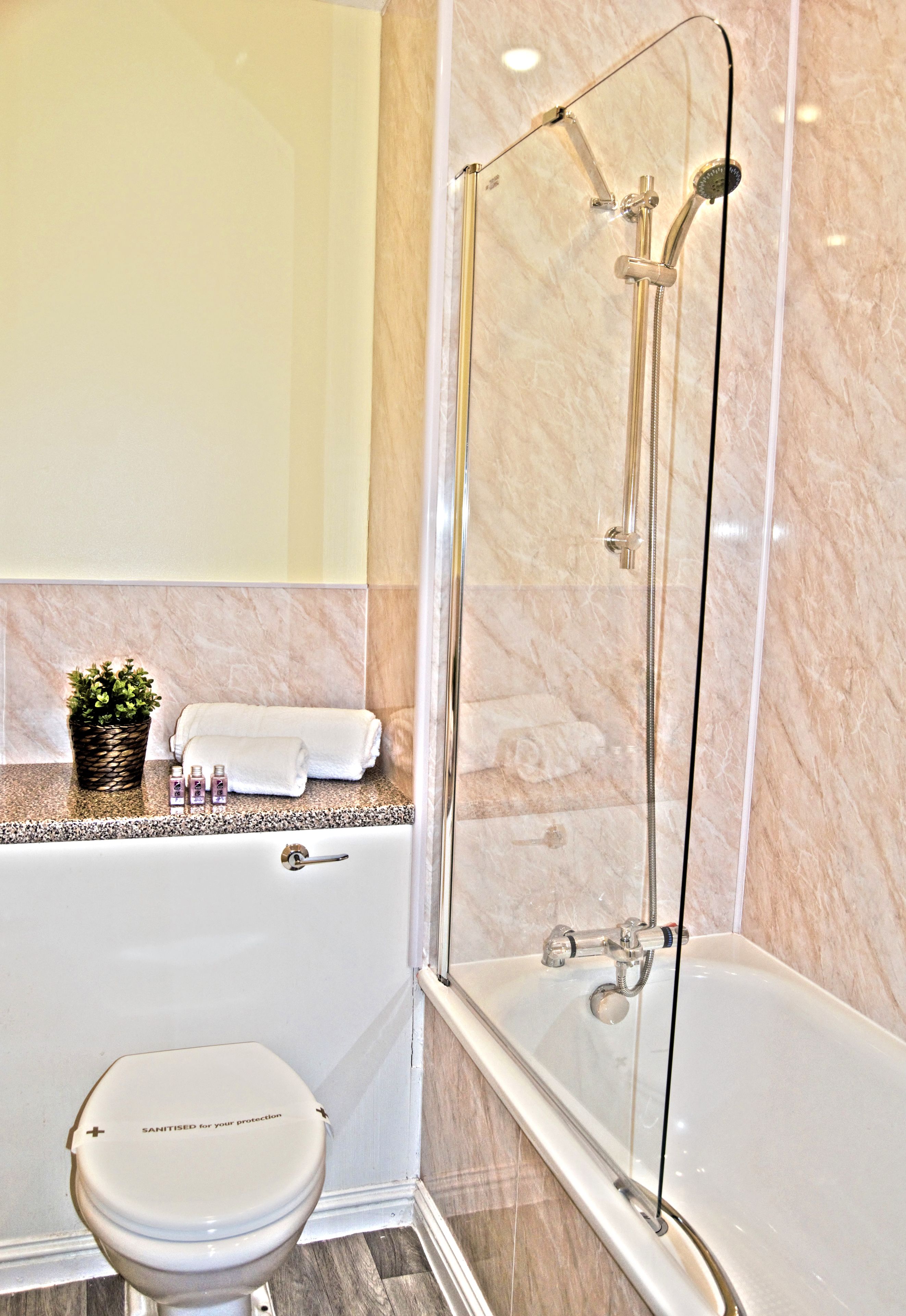 Un baño con ducha de vidrio, inodoro blanco y pared con azulejos de mármol.