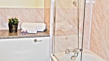 Un baño con ducha de vidrio, inodoro blanco y pared con azulejos de mármol.