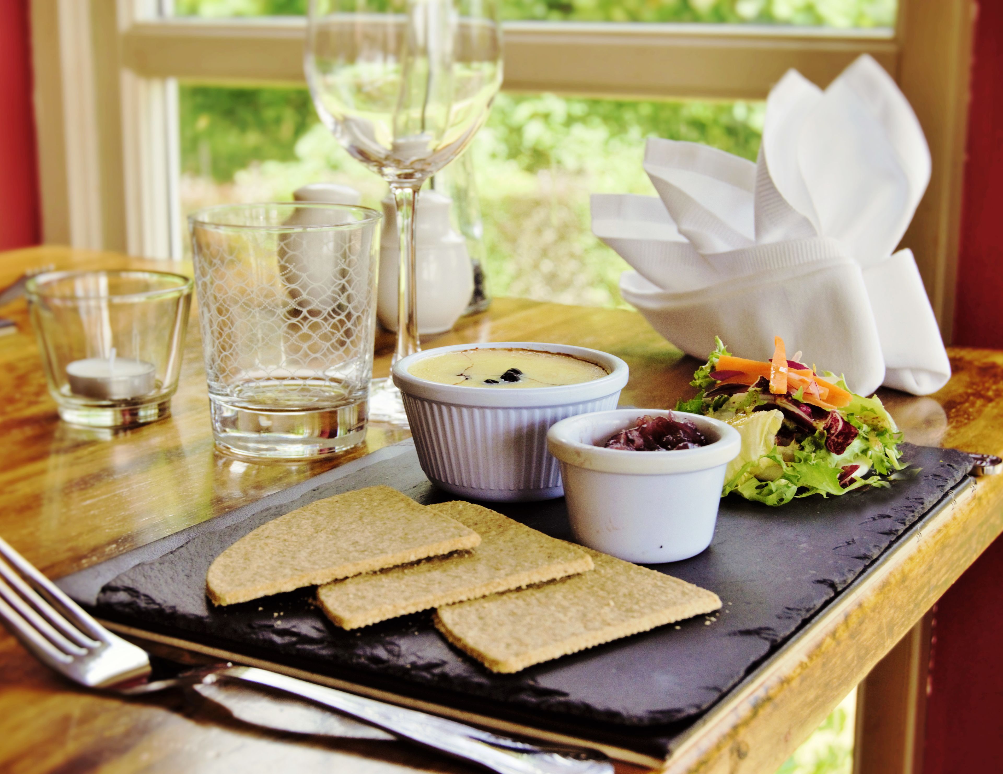 A meal with bread, a salad, and two small bowls of soup on a slate plate.