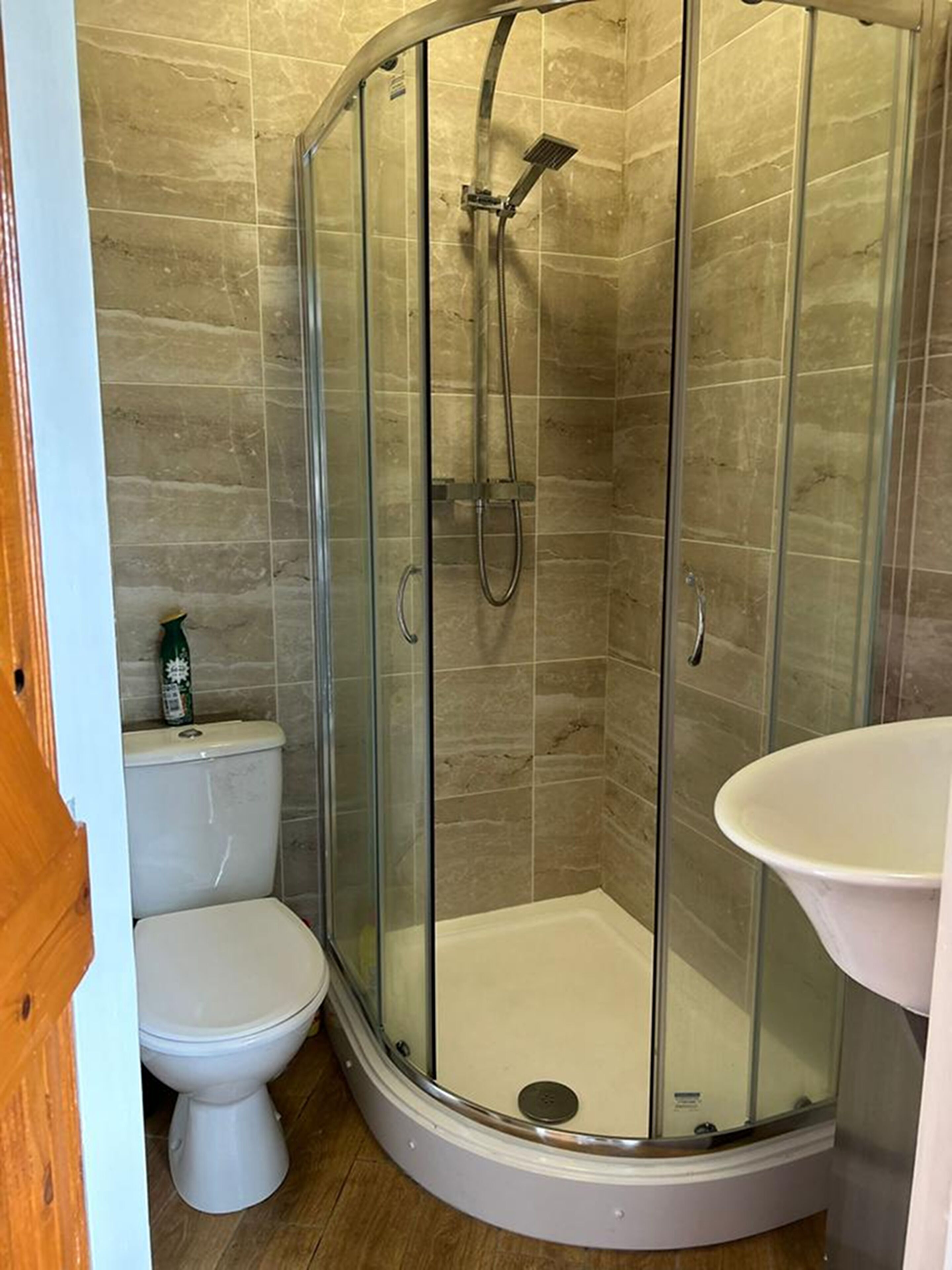 A corner bathroom with a glass-enclosed shower, a toilet, and a sink.