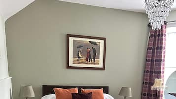 A bedroom with a bed, two bedside tables, a chandelier, a framed picture on the wall, and a window with curtains.
