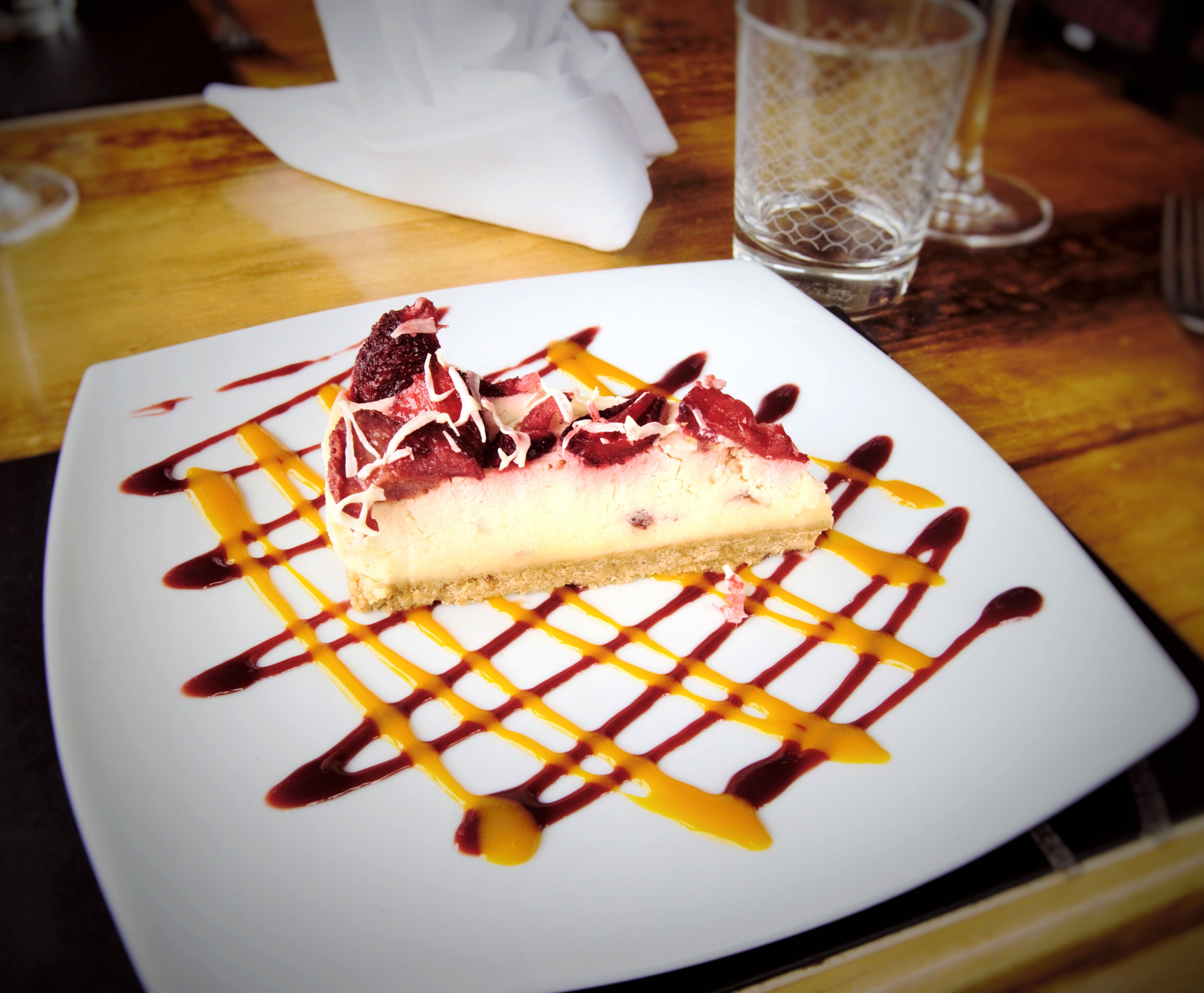 A slice of cheesecake with fruit and sauce on a white plate.