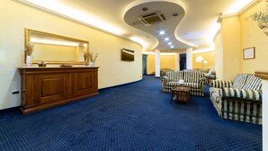A hotel lobby with a curved ceiling, a large mirror, a wooden cabinet, and striped upholstered chairs. - Hotel Hermitage (Polla)