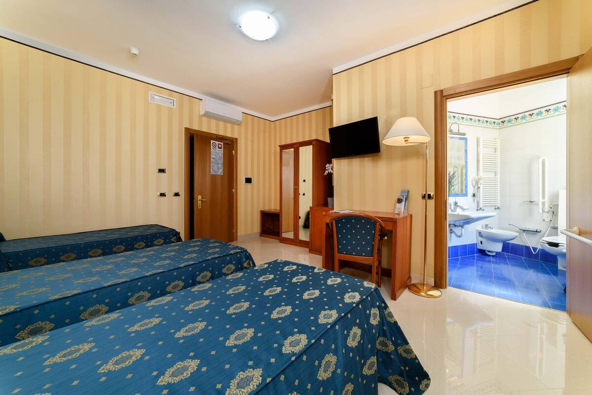 A hotel room with two beds, a desk, a TV, and a bathroom visible through an open door.