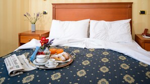 A neatly made bed with white linens, a tray of breakfast including croissants, orange juice, and a newspaper, and a vase with flowers on a bedside table. - Hotel Hermitage (Polla)
