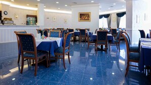 A spacious dining area with blue-tiled floors, wooden chairs, and tables set for dining. - Hotel Hermitage (Polla)