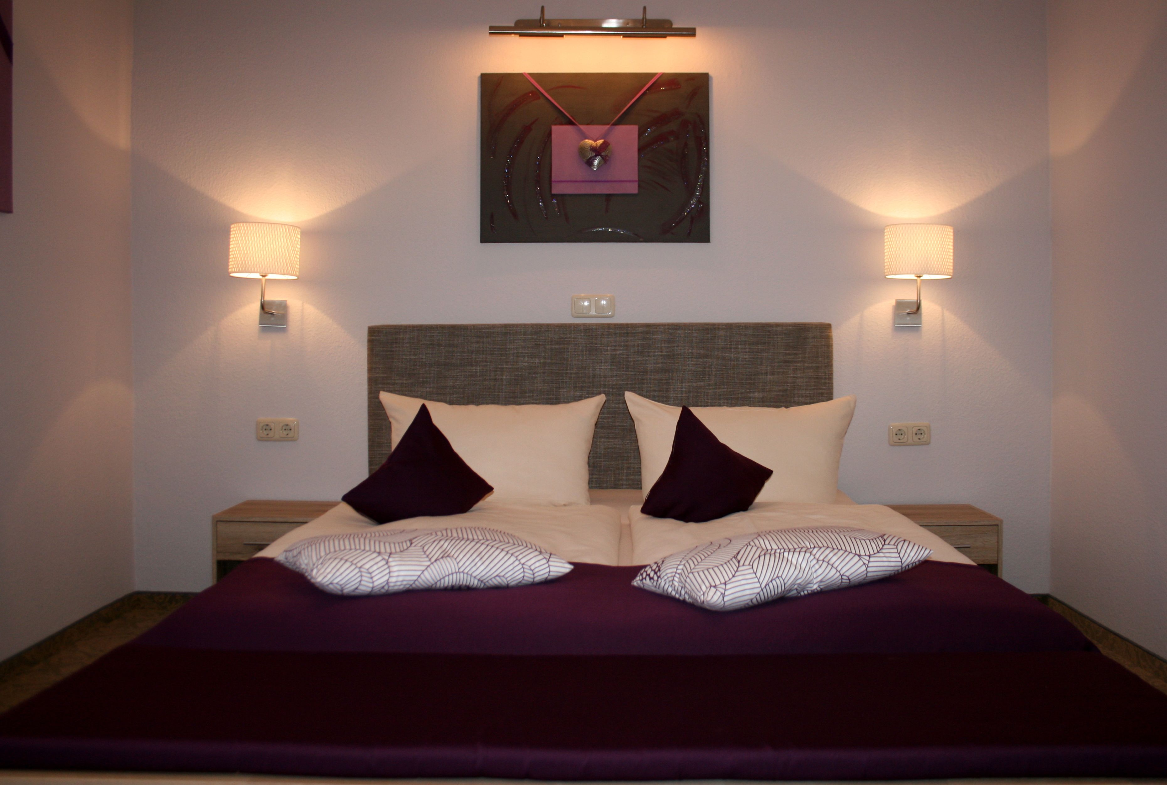 A double bed with a headboard, two bedside tables, and two wall-mounted lamps.