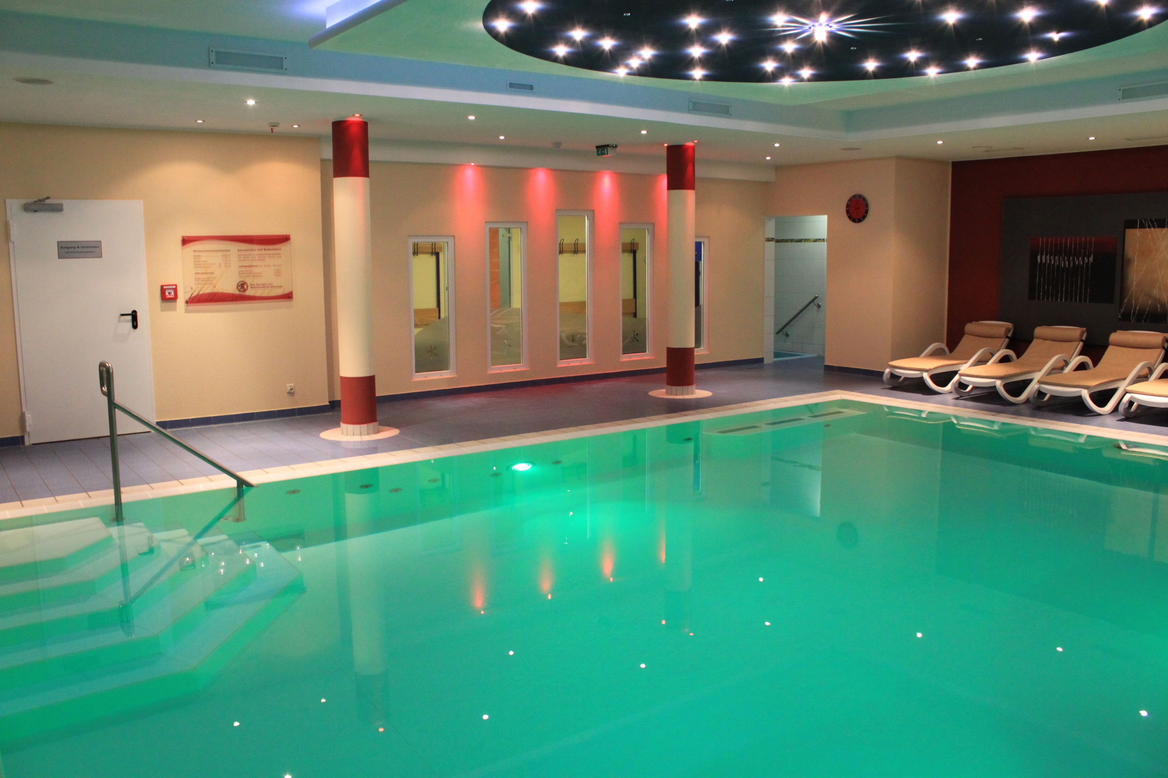 Una piscina con sillas de descanso, un techo con luces que simulan estrellas y una puerta con un cartel.
