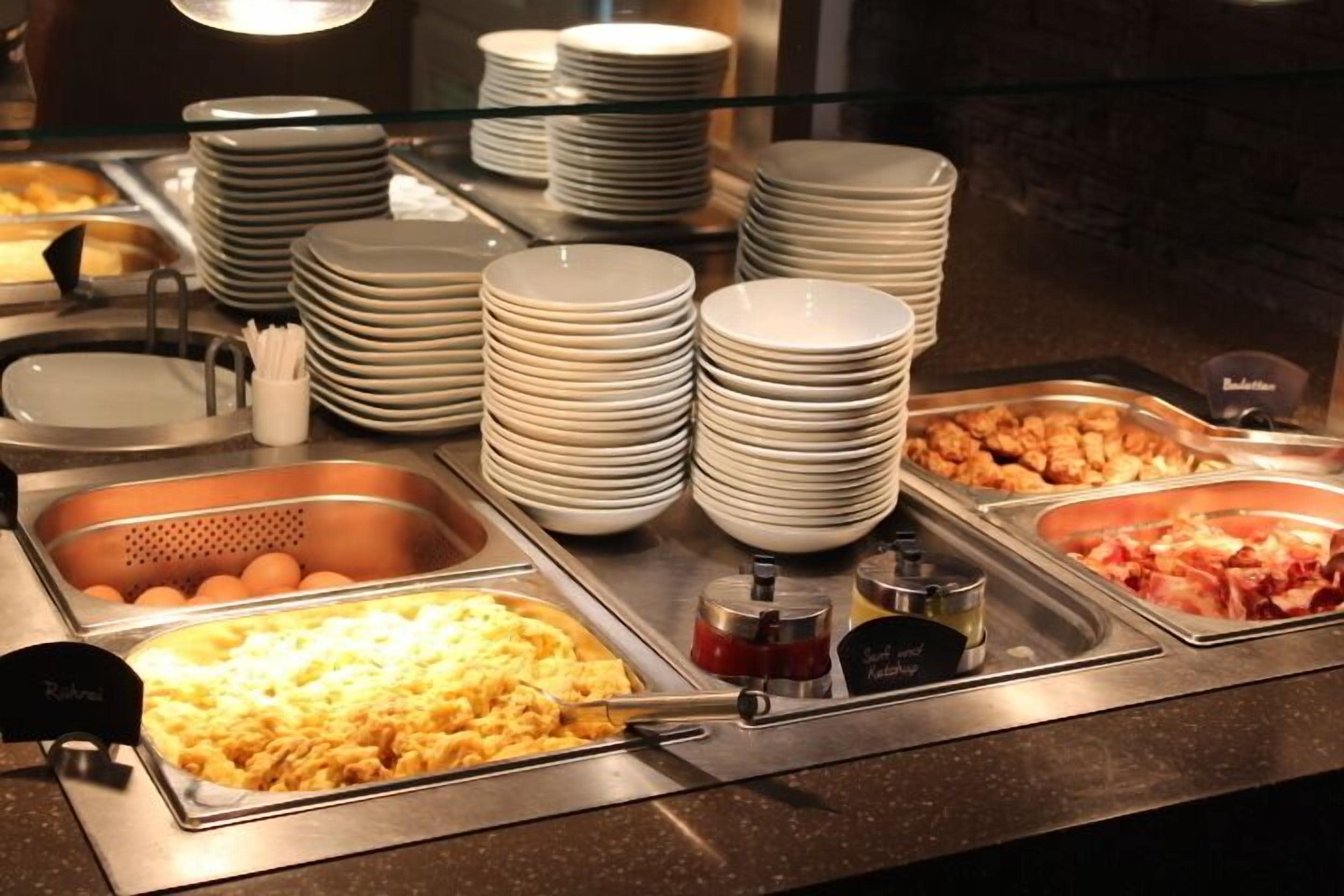 Una barra de buffet con diversos alimentos y platos apilados.