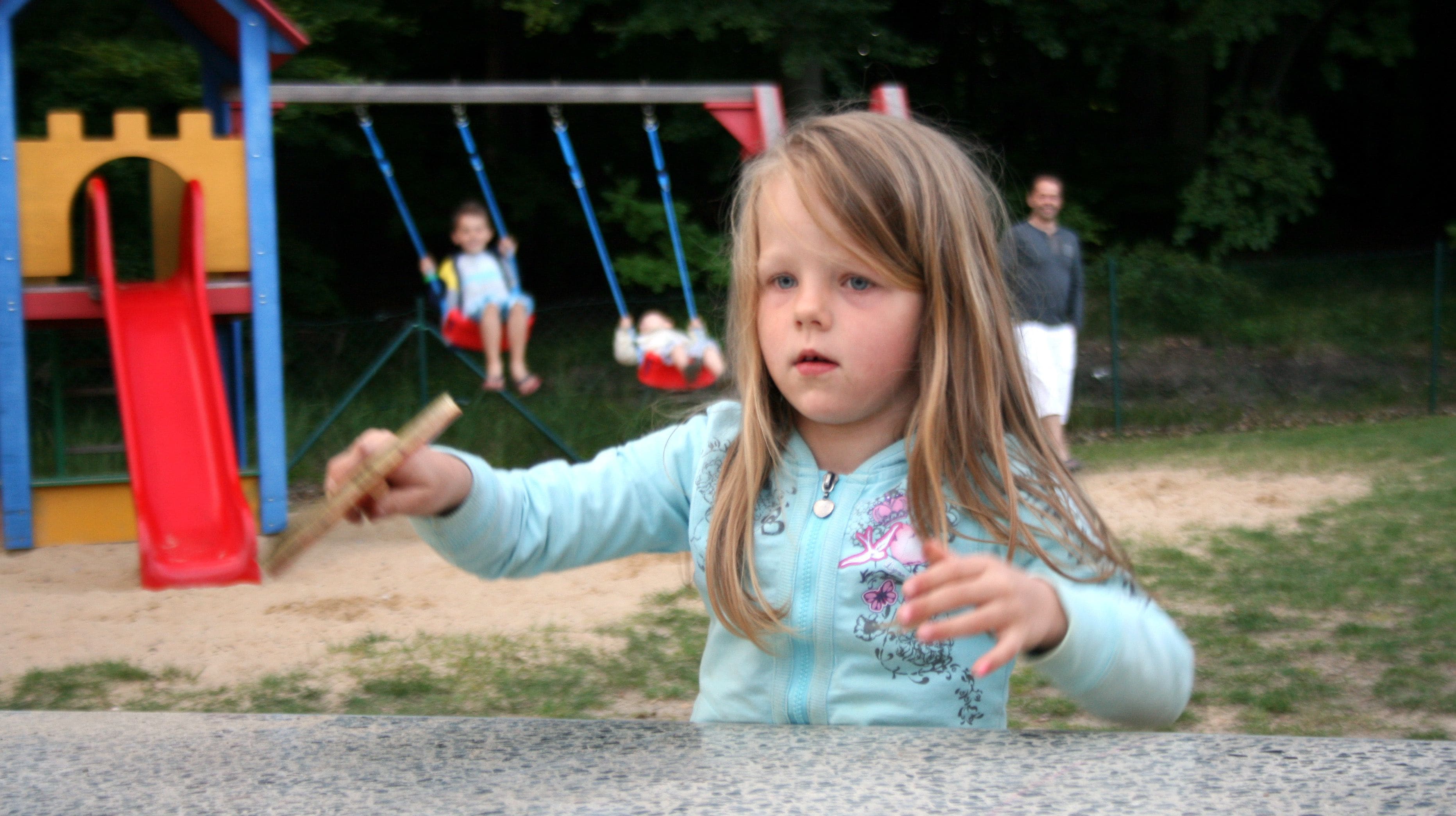 A child at a playground with swings and a slide.