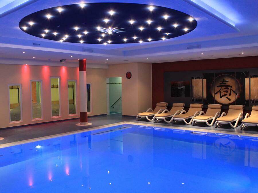 A swimming pool with lounge chairs, a ceiling with star-like lights, and a wall with a large Chinese character.
